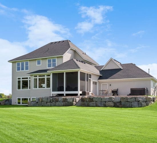 Angled rear view of a custom home with screened porch and stone retaining wall