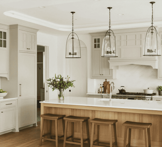 Bright white kitchen with wood island, stools, and pendant lights
