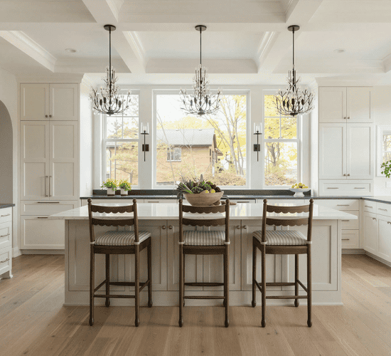 Bright white kitchen with island, stools, chandeliers, and large windows