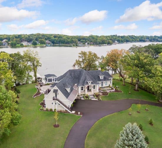Aerial view of lakeside home with landscaped grounds and driveway