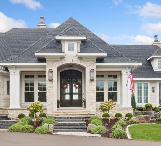 Elegant stone house entrance with American flag and landscaped garden
