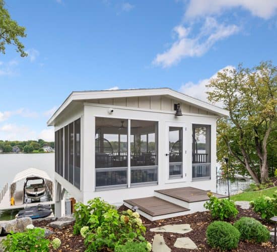 Screened lakeside boathouse beside docked boats and landscaped garden