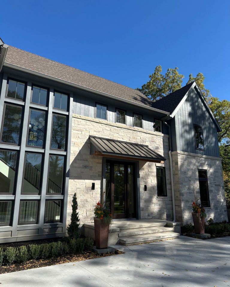 Modern home with stone and metal exterior, large windows, and landscaped entrance.